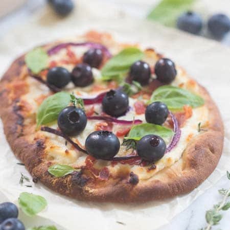 A crisp blueberry pizza garnished with basil leaves.