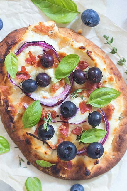 A pizza made on naan bread with blueberries, pancetta, red onion and basil.