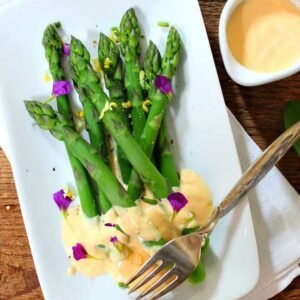 square photo of lemon butter sauce drizzled over asparagus stalks on a white plate