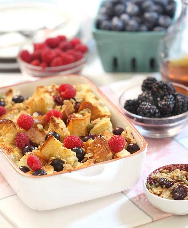 A pan of baked french toast surrounded by bowls of berries.