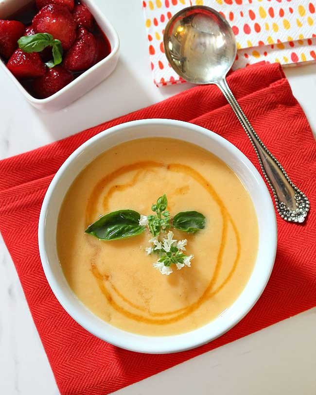 Cantaloupe Soup on a red napkin with a small box of strawberries next to it and a silver spoon