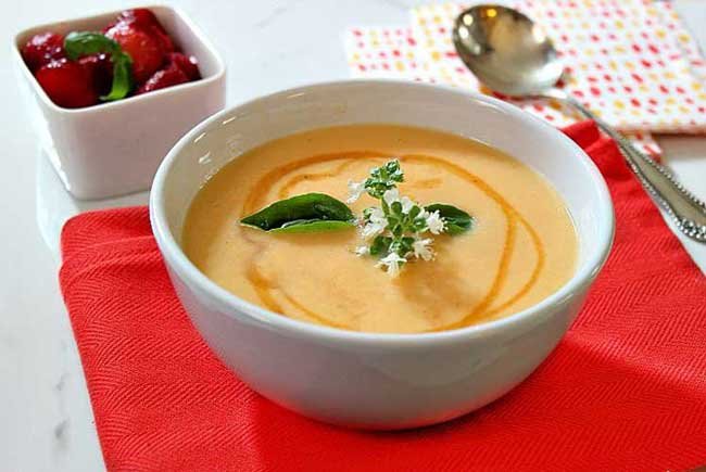 cantaloup soup on a red napkin with a small box of strawberries next to it and a silver spoon
