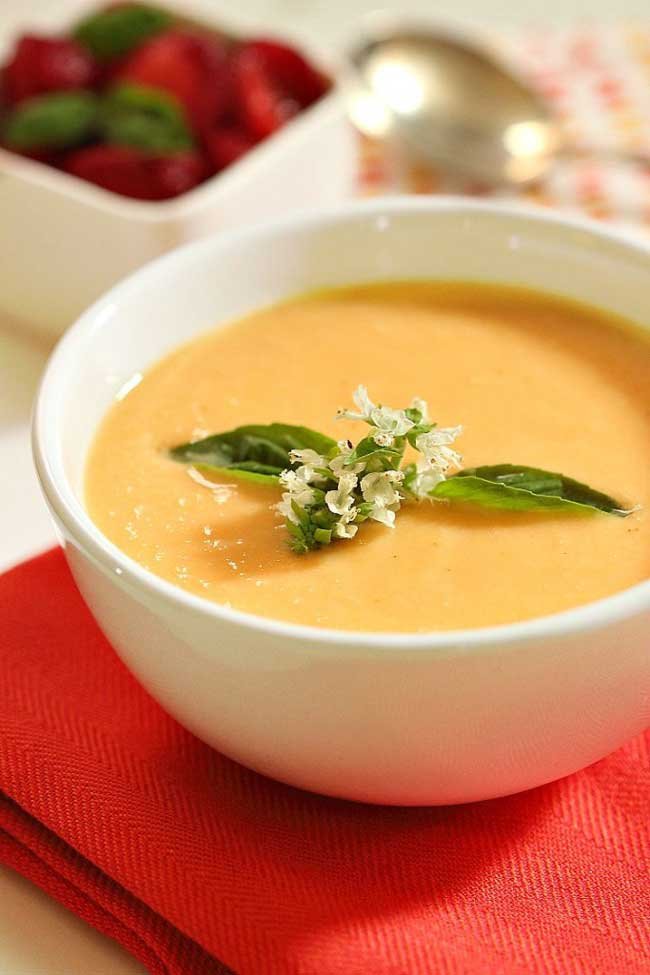 Cantaloupe Soup on a red napkin with a small box of strawberries next to it and a silver spoon