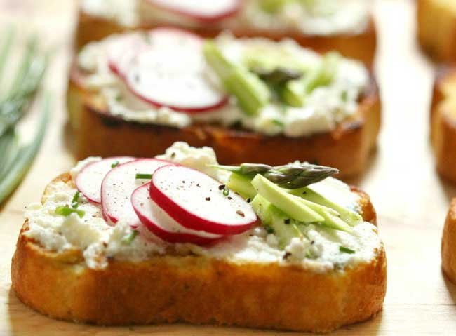 Two slices of Garlic Crostini topped with ricotta, asparagus and radishes.