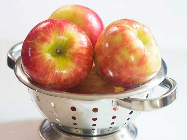 A silver colander filled with fresh honey crisp apples.