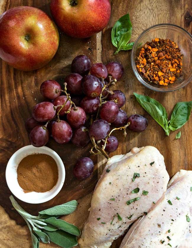 chicken breast, grapes & spices on a cutting board.