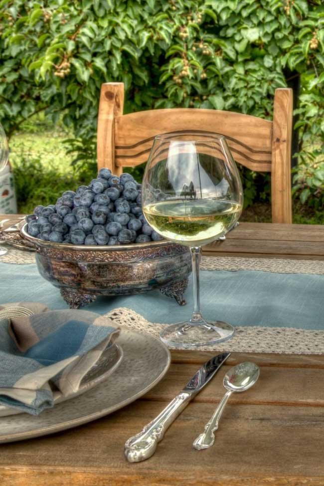 a table set outdoors with a glass of white wine and a bowl of fresh blueberries