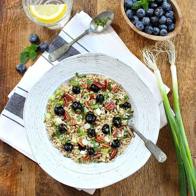 square overhead photo of quinoa lentil salad with a small bowl of blueberries and a glass of water with lemon