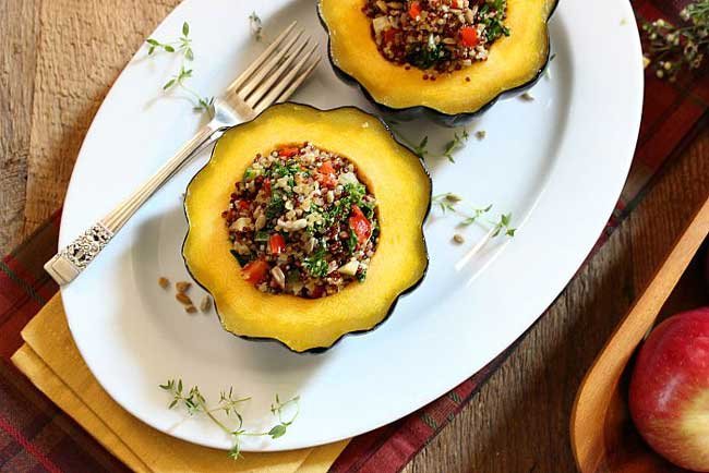 2 quinoa stuffed acorn squash halves on a oval white plate with a silver fork