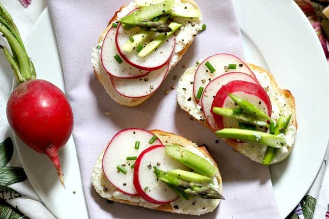 Three slices of ricotta crostini shows from overhead topped with radishes.