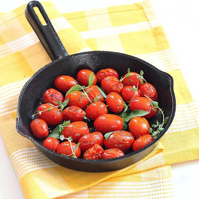 roasted grape tomatoes with herbs on a skillet on a yellow and white cloth