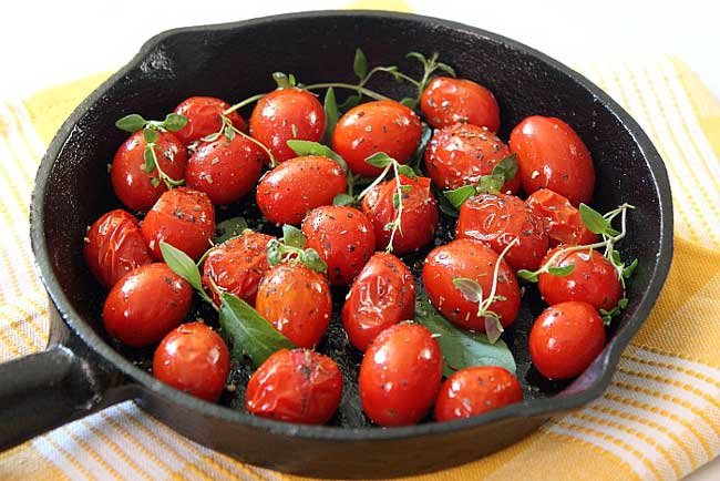 closeup photo of roasted grape tomatoes with herbs on a skillet on a yellow and white cloth