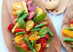close up of tomato basil salad with green beans on a wooden plate