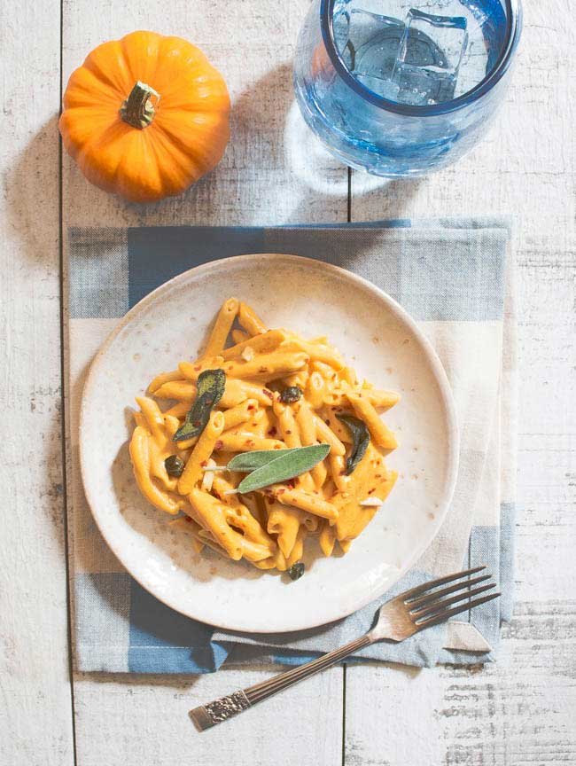 overhead shot of vegan pumpkin pasta on a set table with a small pumpkin in the corner