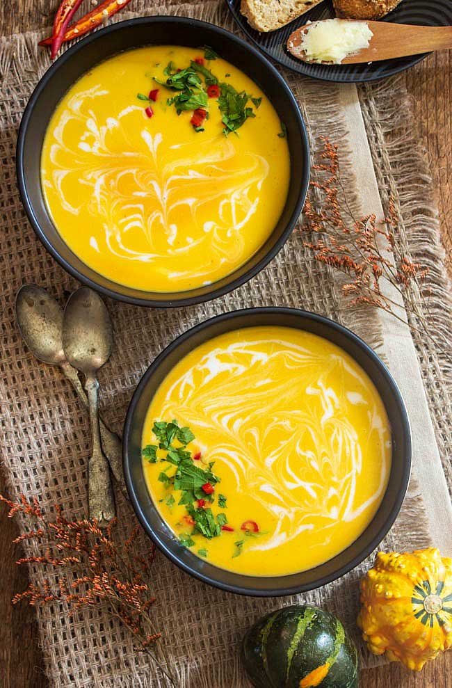 overhead shot of 2 bowls of Vegetarian Butternut Squash Soup with 2 silver spoons on the table.