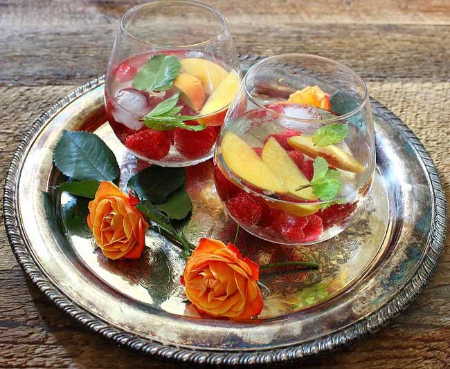 2 glasses of a wine spritzer recipe with peaches and raspberries