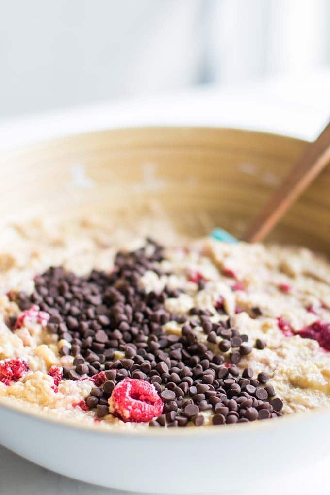 A bowl of banana bread batter with raspberries and dark chocolate chips.